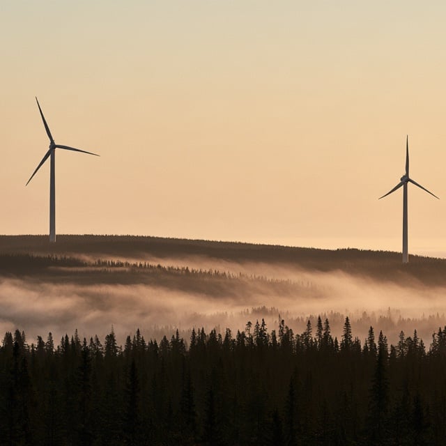 Two wind turbines above a misty forest at dawn