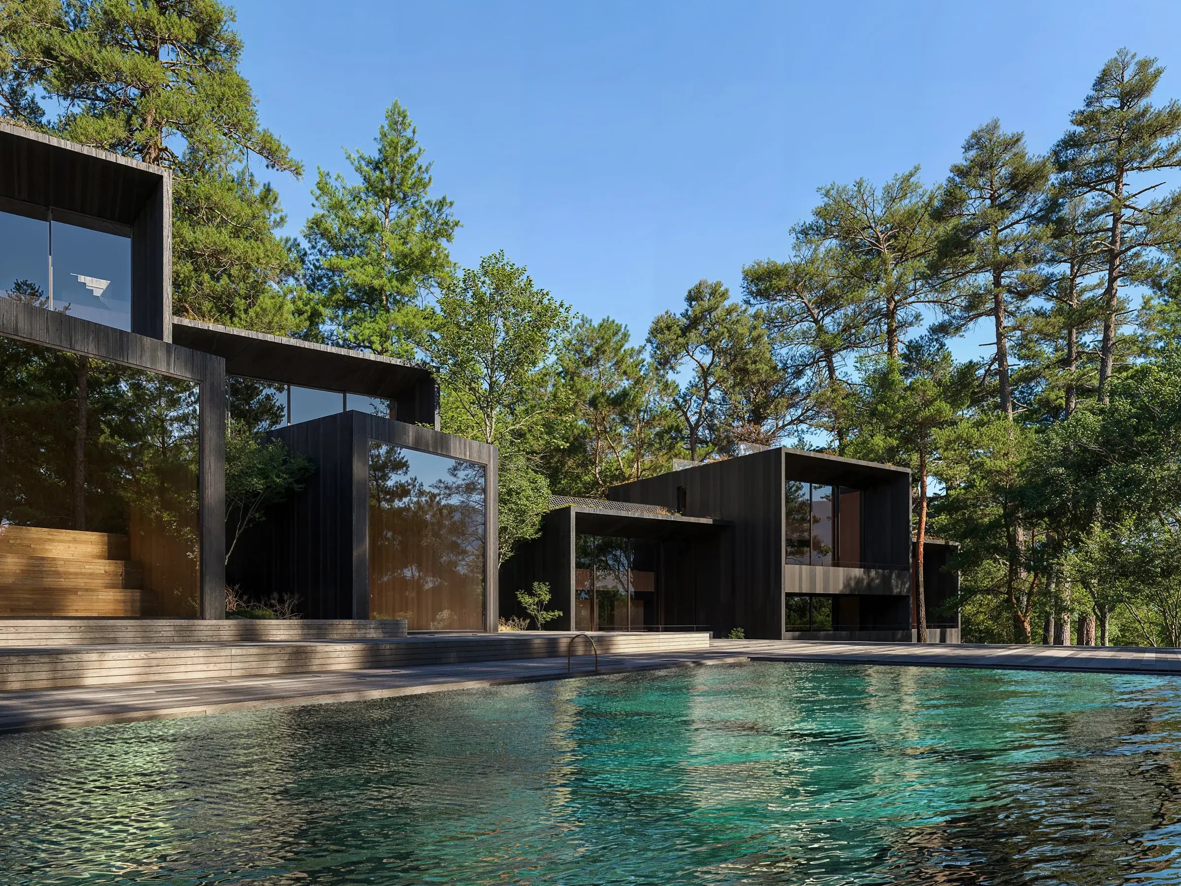 Black timber houses among tall pines beside a turquoise pool