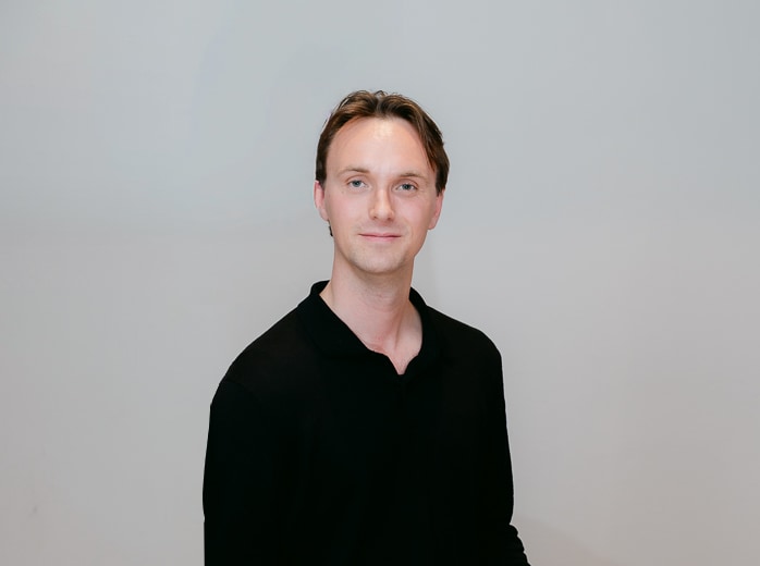Portrait of a Verumatic team member in a black shirt, seated against a pale wall